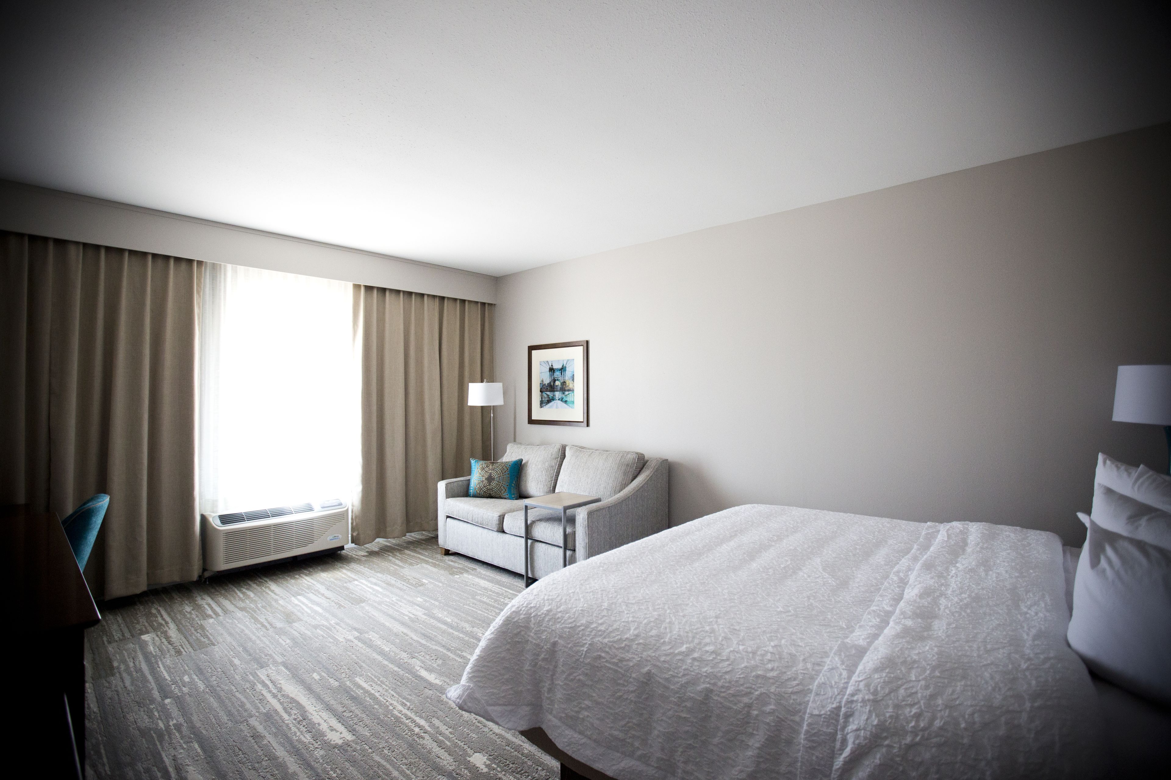 A hotel room with a large bed, a sofa, a desk, and a window with curtains.