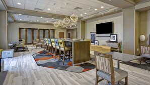 A modern hotel lobby with a central island, multiple seating areas, and a large flat-screen TV on the wall. - Hampton Inn Blue Ash/Cincinnati (Cincinnati)