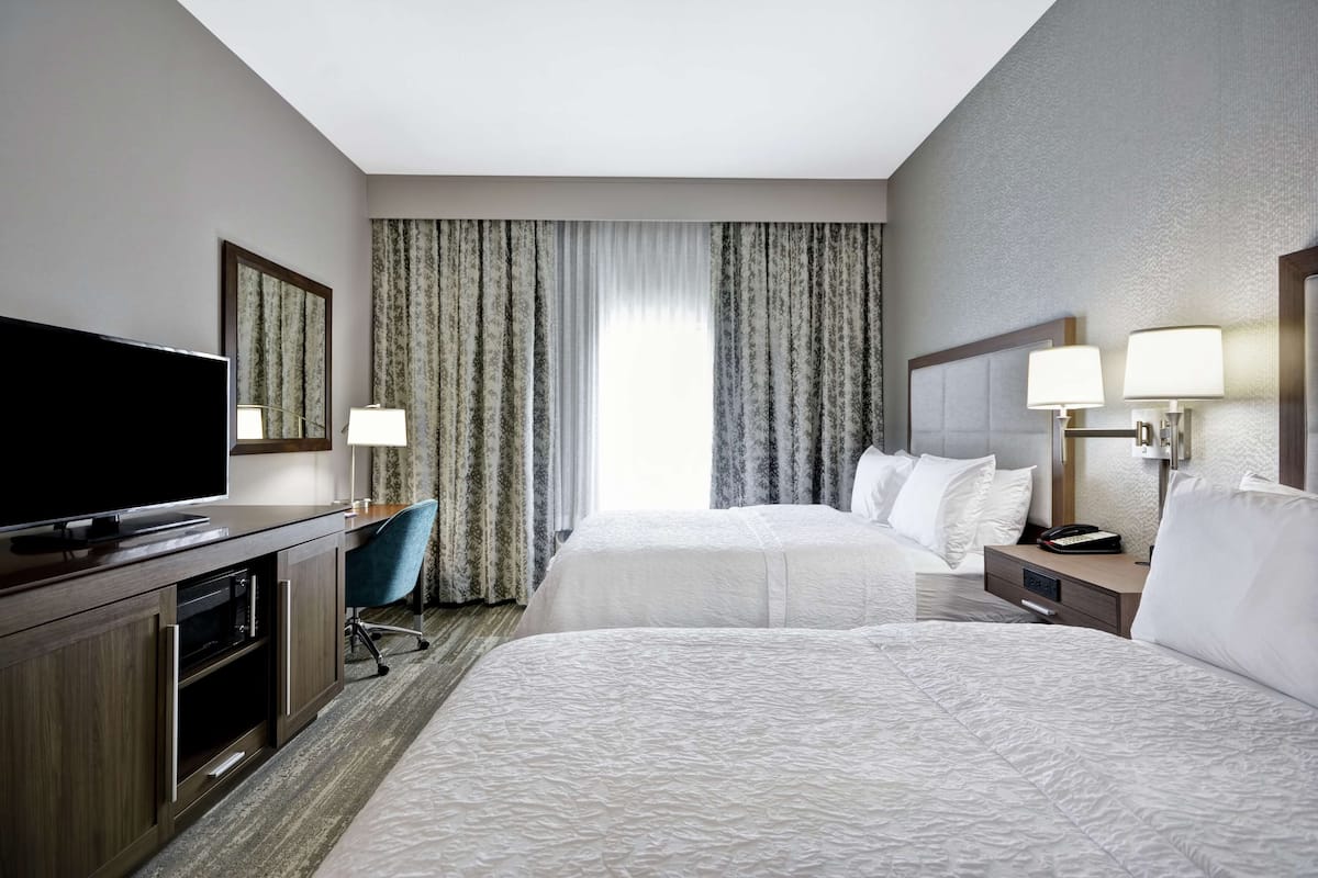 A hotel room with two beds, a TV, a desk, and a chair.