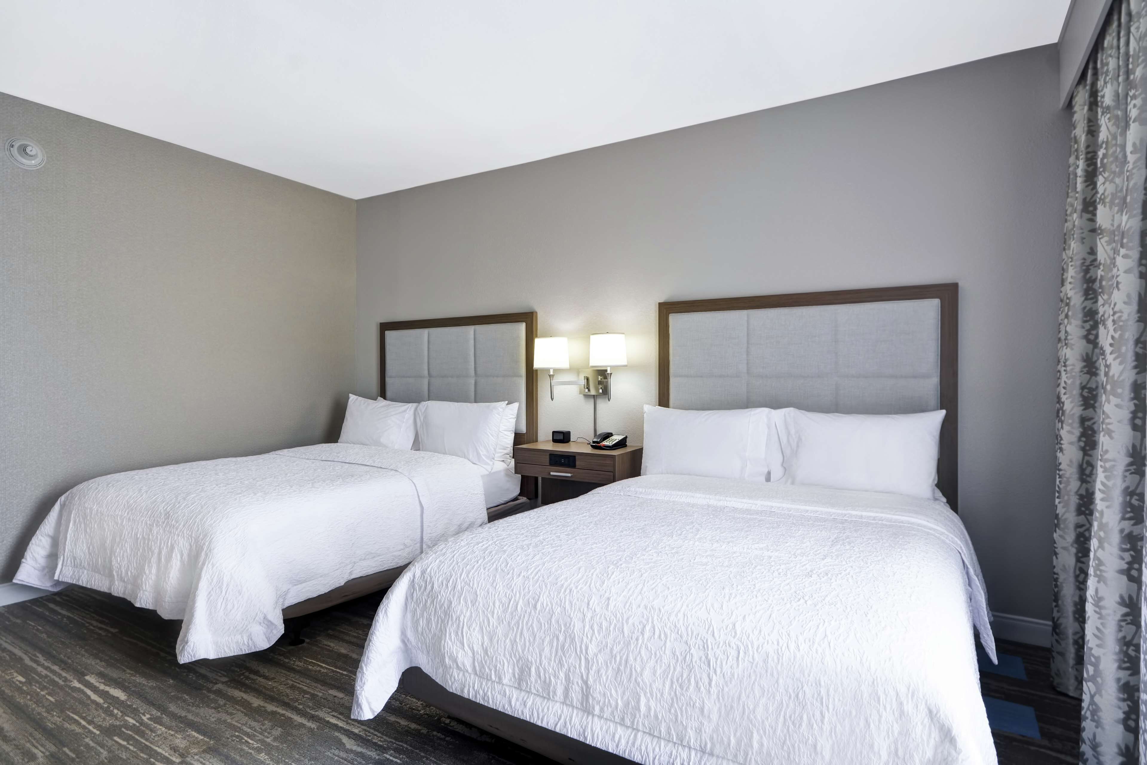 A hotel room with two beds, a nightstand with lamps, and a window with curtains.