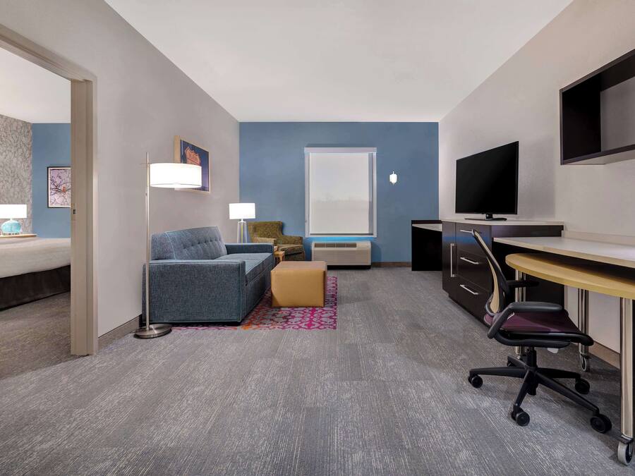 A hotel room with a bed, a sofa, a desk, a TV, and a window.