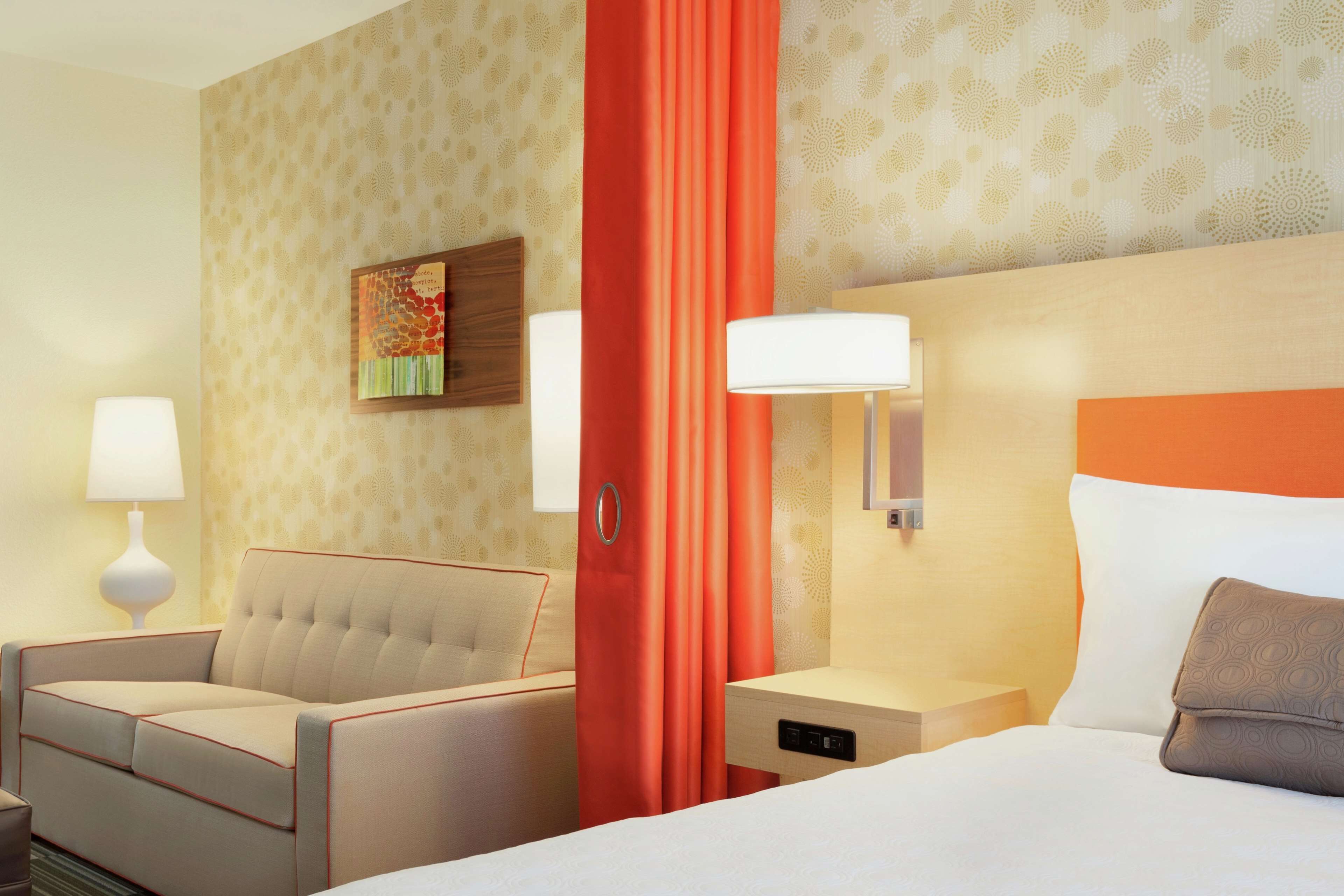 A hotel room with a bed, a sofa, a nightstand, a lamp, and a painting on the wall.