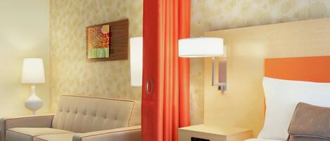 A hotel room with a bed, a sofa, a nightstand, a lamp, and a painting on the wall.