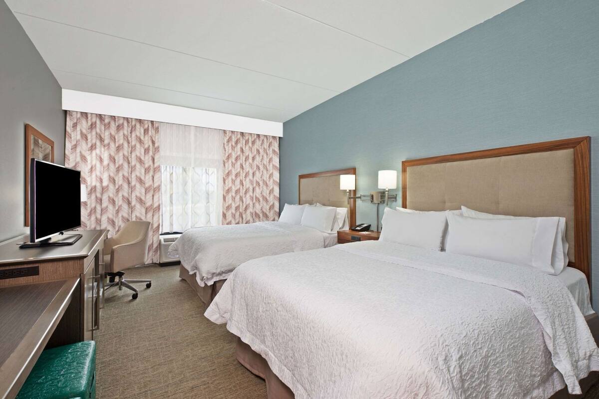 Ein Hotelzimmer mit zwei Betten, einem Schreibtisch mit Fernseher und einem Sessel.