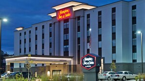 Un hôtel Hampton Inn & Suites doté d’une façade moderne, de plusieurs étages et d’une enseigne au néon bien visible.