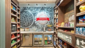 L'intérieur d'un magasin, avec des étagères remplies de collations et de boissons, et un comptoir central sur lequel est affiché un panneau indiquant « Friandises ».