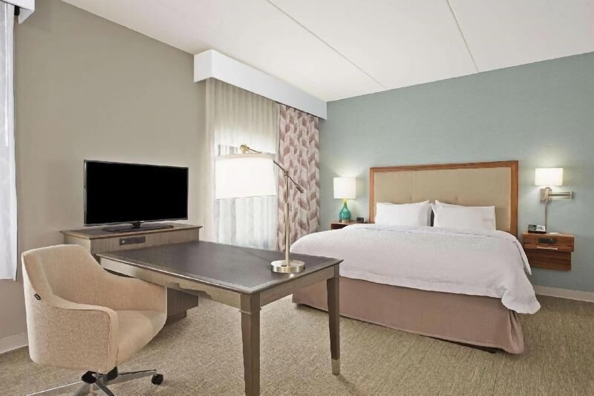 Habitación de hotel con cama, escritorio con televisor, una silla y mesita de noche con lámparas.
