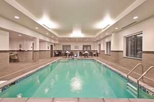 Una amplia piscina interior con borde de azulejos, rodeada por un espacio de tonos neutros, techo alto e iluminación empotrada.