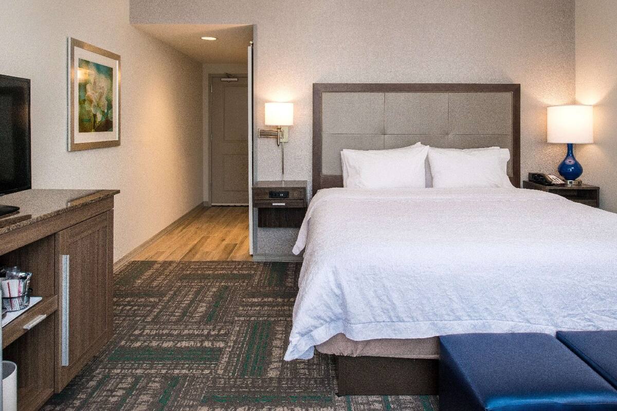 Ein Hotelzimmer mit Bett, Nachttischen, Fernseher und einem Bild an der Wand.