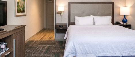 A hotel room with a bed, bedside tables, a TV, and a painting on the wall.