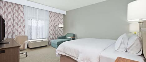 A hotel room with a bed, a desk, a chair, and a window with curtains.