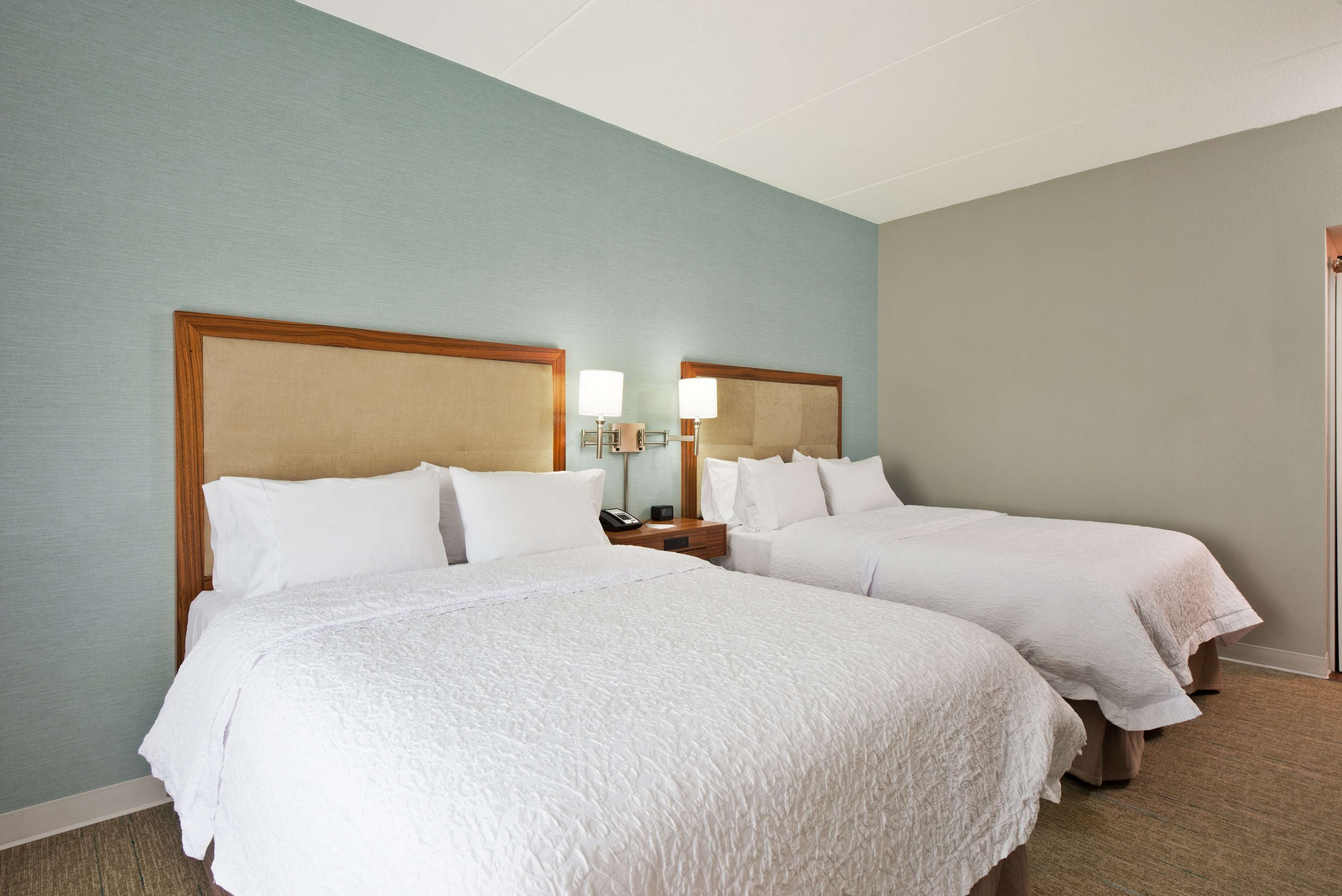 Habitación de hotel con dos camas, cada una con cabecero de madera, ropa de cama blanca y lámparas de noche.