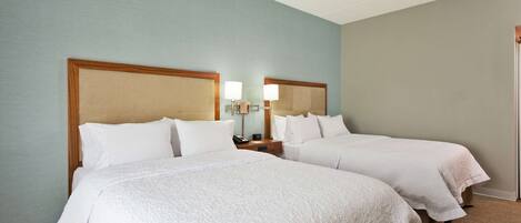 Habitación de hotel con dos camas, cada una con cabecero de madera, ropa de cama blanca y lámparas de noche.