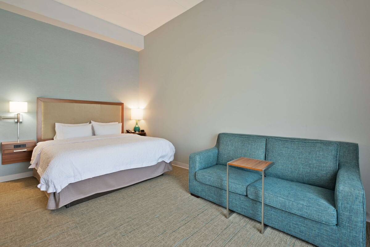 Ein Hotelzimmer mit einem Bett, einem Nachttisch, einer Lampe und einem türkisblauen Sofa.