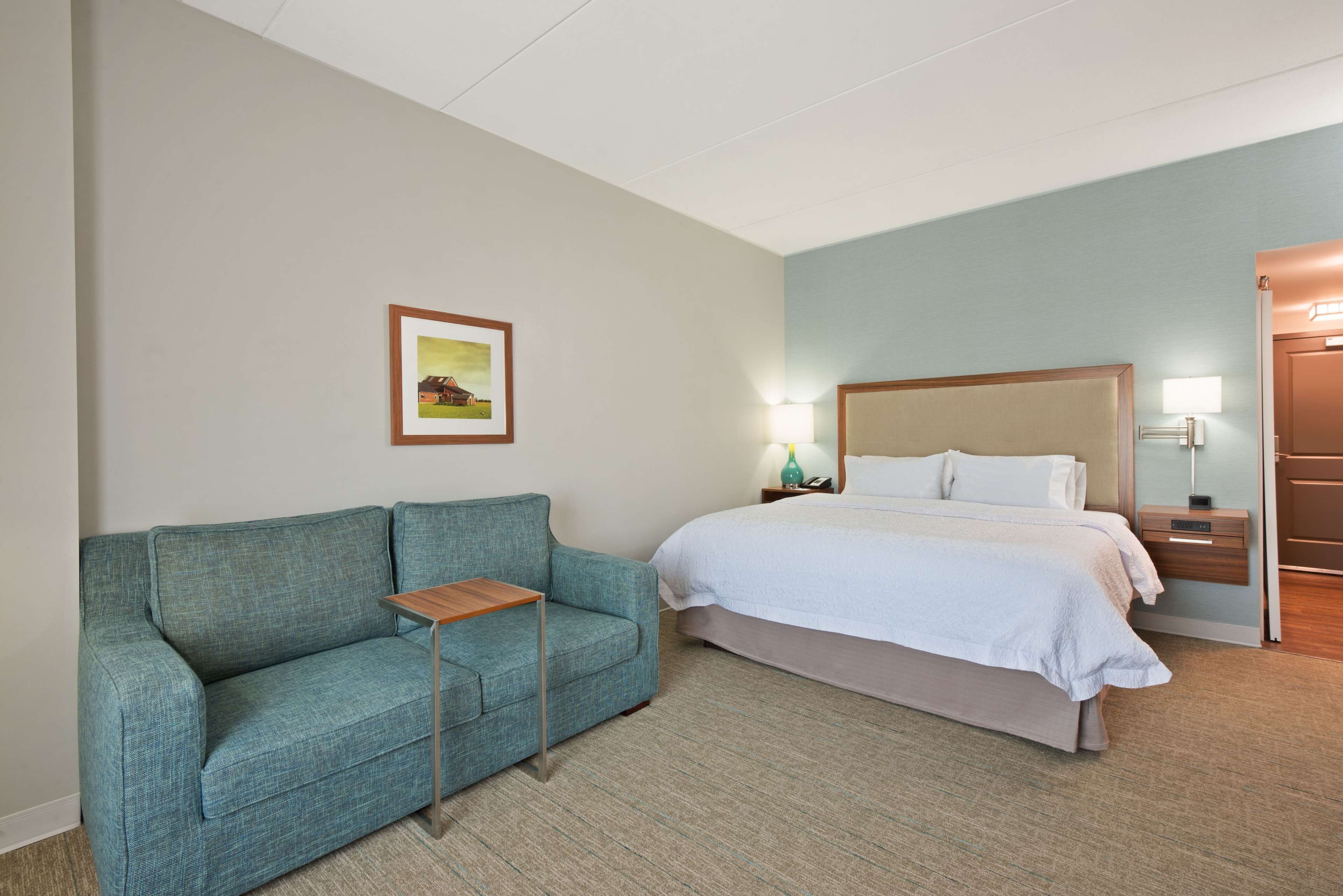 A hotel room with a bed, a sofa, a bedside table, and a nightstand with a lamp.