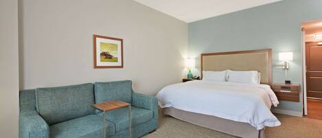 A hotel room with a bed, a sofa, a bedside table, and a nightstand with a lamp.