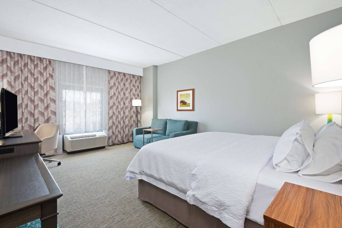 Ein Hotelzimmer mit Bett, Schreibtisch, Stuhl, Lampe und einem Bild an der Wand.