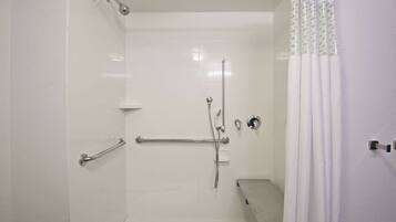 Um chuveiro com entrada livre, pequeno e branco, com porta de vidro, chuveiro manual e assento de vidro.
