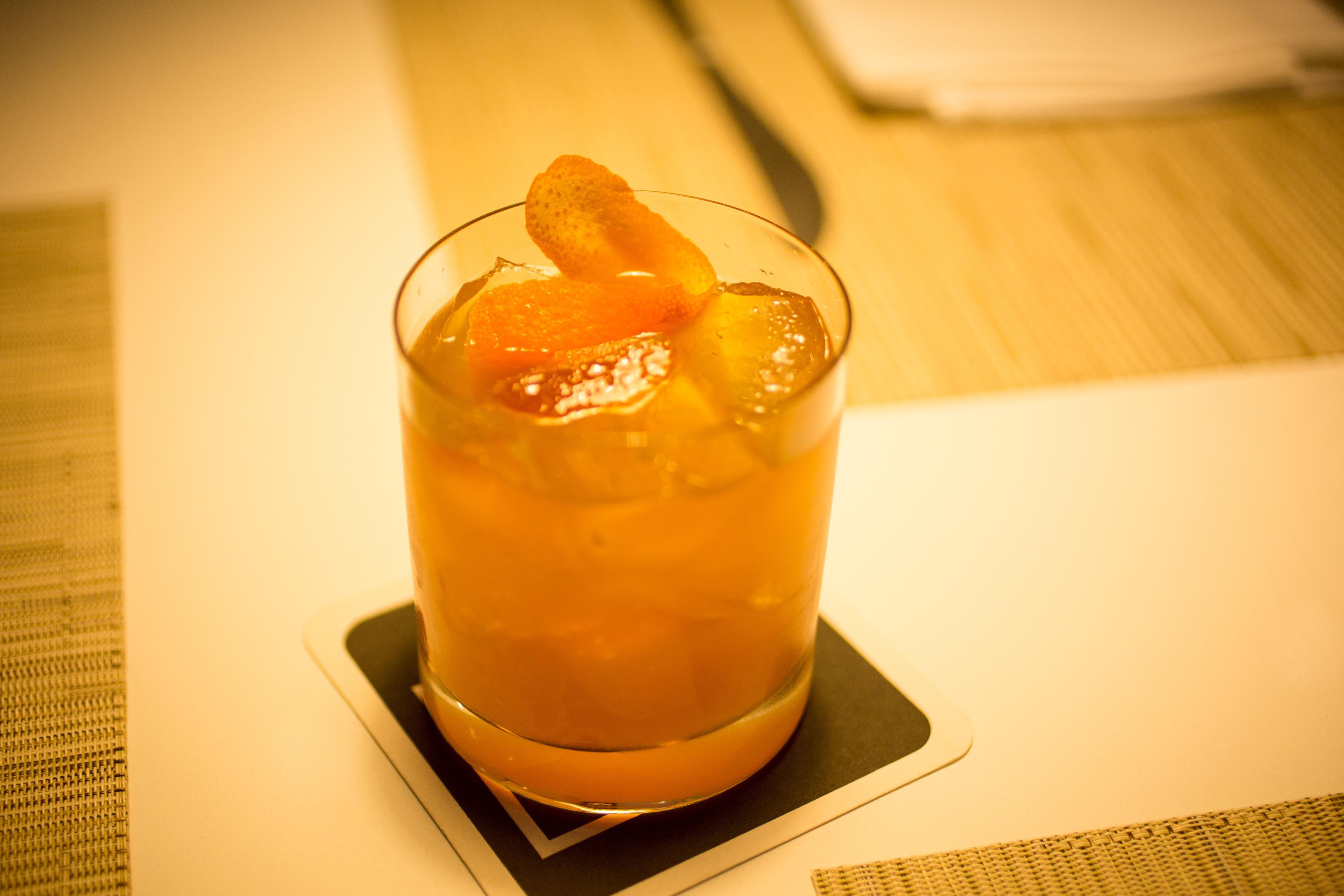 A glass with a beverage and a slice of orange on a coaster.