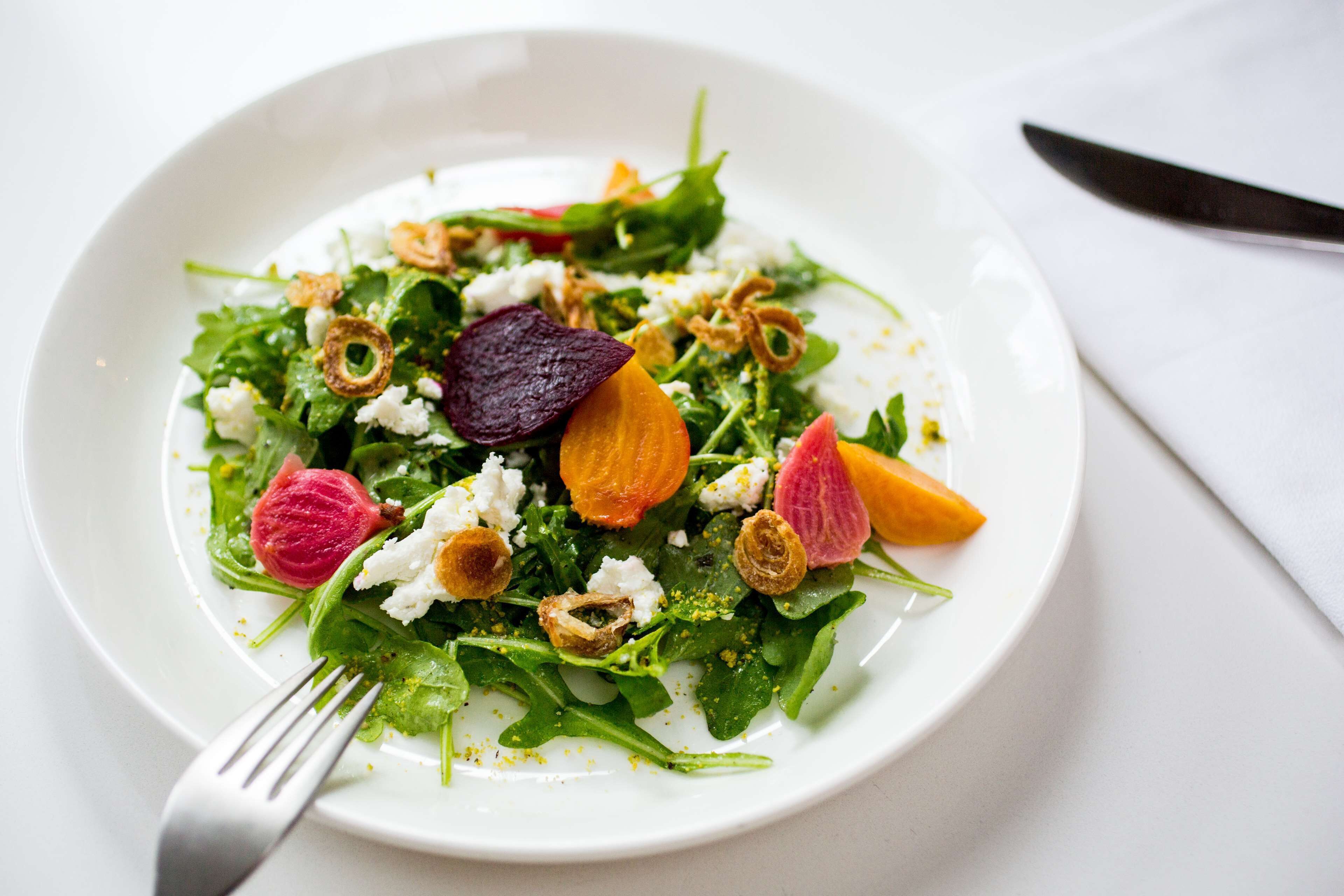 A white plate with a salad containing greens, beets, and croutons.