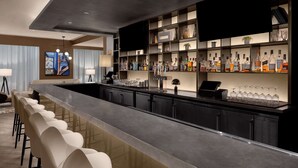 A modern bar area with a long counter, bar stools, and a variety of liquor bottles. - Hilton Brooklyn New York (Brooklyn)