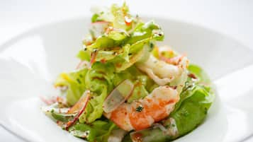 Une assiette blanche contenant une salade composée de laitue, de radis et de crevettes.