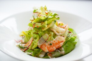 A white plate with a salad consisting of lettuce, radish, and shrimp.