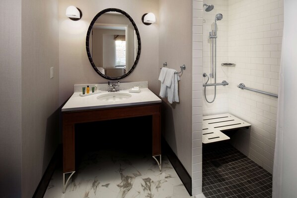 A bathroom with a sink, mirror, towel rack, and shower area.