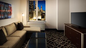 A modern hotel room with a sofa, a coffee table, a TV, and a window with a city view. - Hilton Brooklyn New York (Brooklyn)
