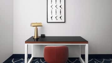 A desk with a lamp, a framed picture, and a chair in a room with patterned carpet.