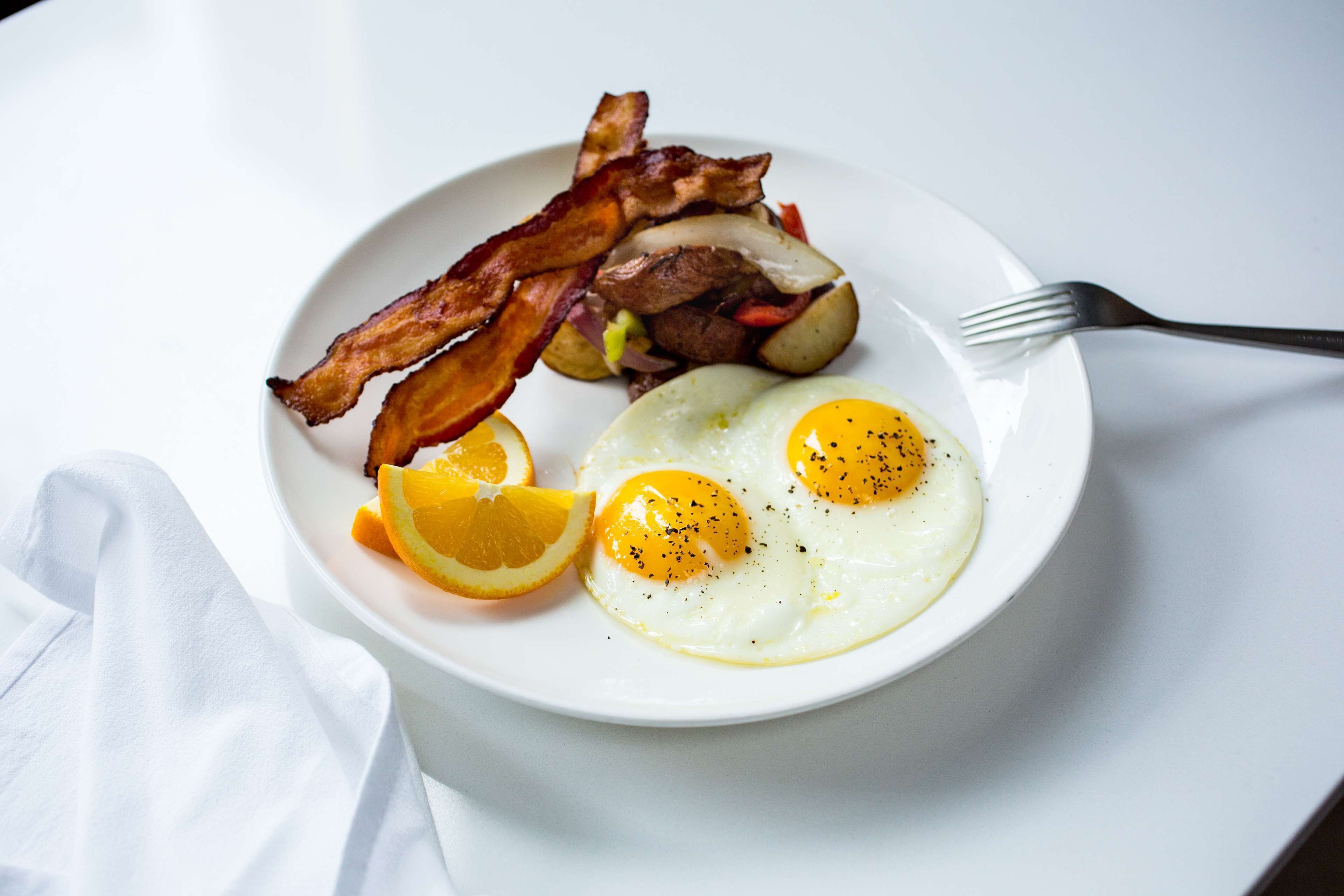 Une assiette avec des œufs, du bacon, des pommes de terre et une tranche d’orange.