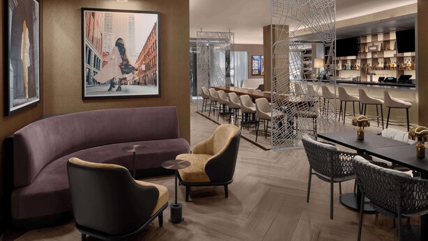 A modern lounge area with a curved sofa, armchairs, a dining table, and a bar area with stools. - Hilton Brooklyn New York (Brooklyn)