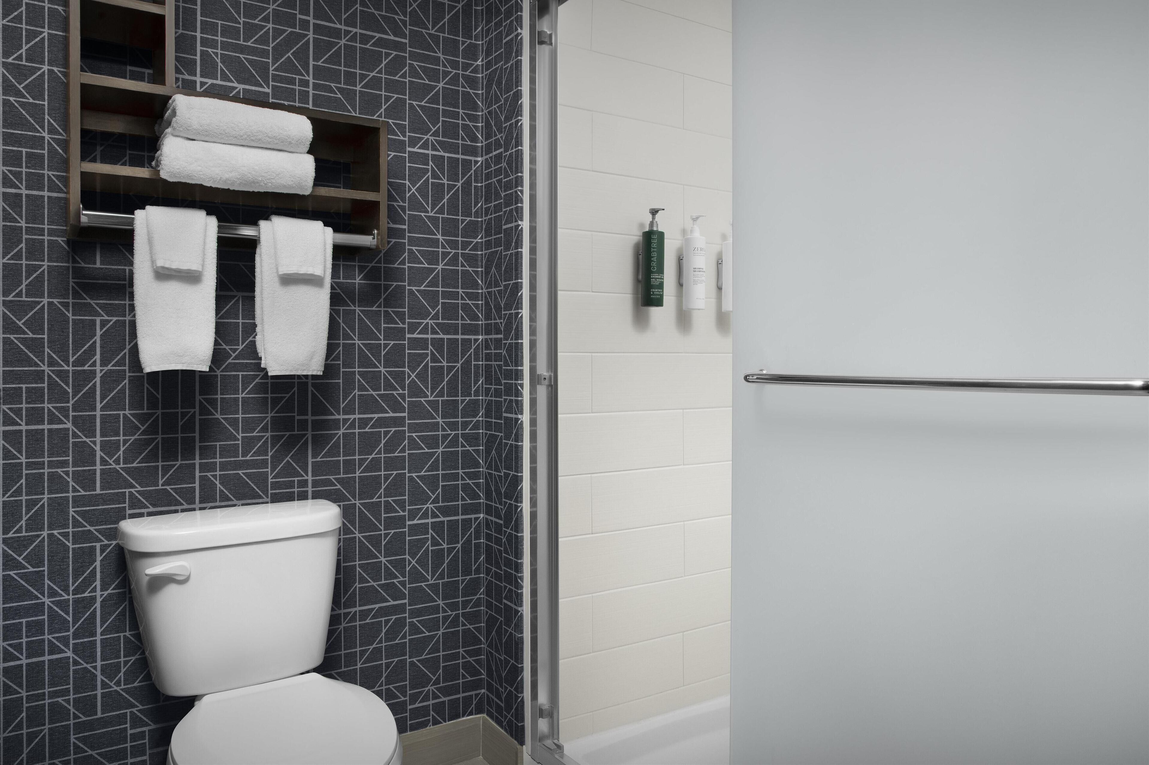 Et badeværelse med moderne design, der indeholder toilet, et håndklædestativ med foldede håndklæder og en bruseniche.