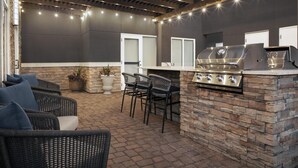 An outdoor patio with stone walls, a grill, and wicker chairs.