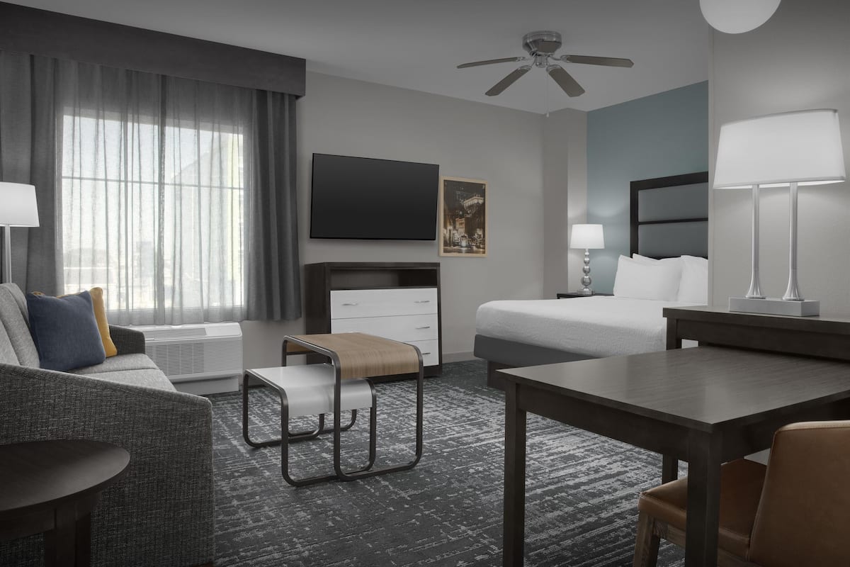 Ein modernes Hotelzimmer mit einem Bett, einer Couch, einem Schreibtisch, einem Stuhl, einem Fernseher und einem Deckenventilator.