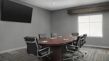 A conference room with a large table, six chairs, a projector screen, and a large window.