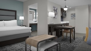 A modern hotel room with a bed, desk, chair, and a small table.