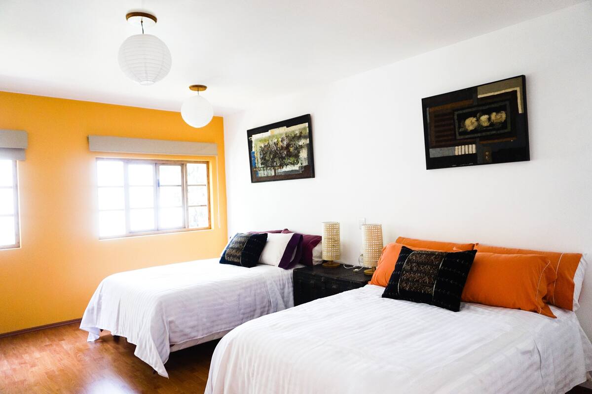 A room with two beds, a window, and a wall-mounted picture.