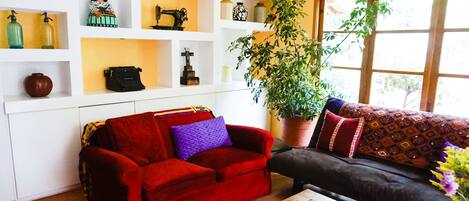Una sala de estar con un sofá rojo y negro, una mesa de centro de madera y un estante blanco con varios objetos decorativos.