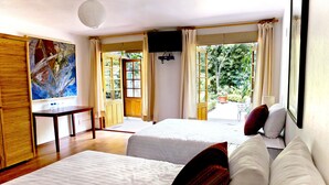 A hotel room with two beds, a desk, a TV, and large windows with curtains. - Casa Jacinta Guest House (Mexico City)