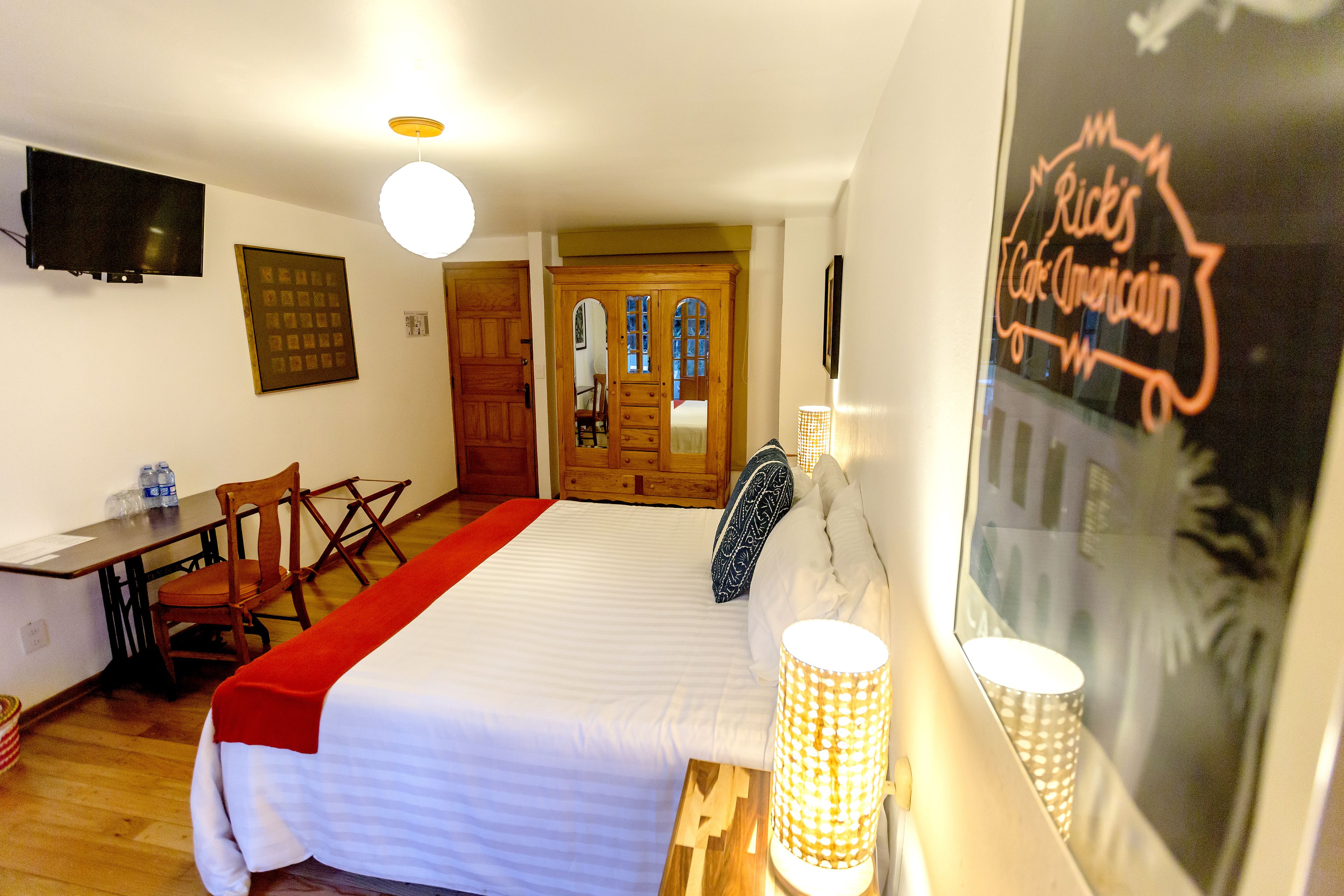 A hotel room with a bed, a desk, a chair, a TV, and a door leading to another room.