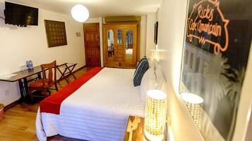 A hotel room with a bed, a desk, a chair, a TV, and a door leading to another room.