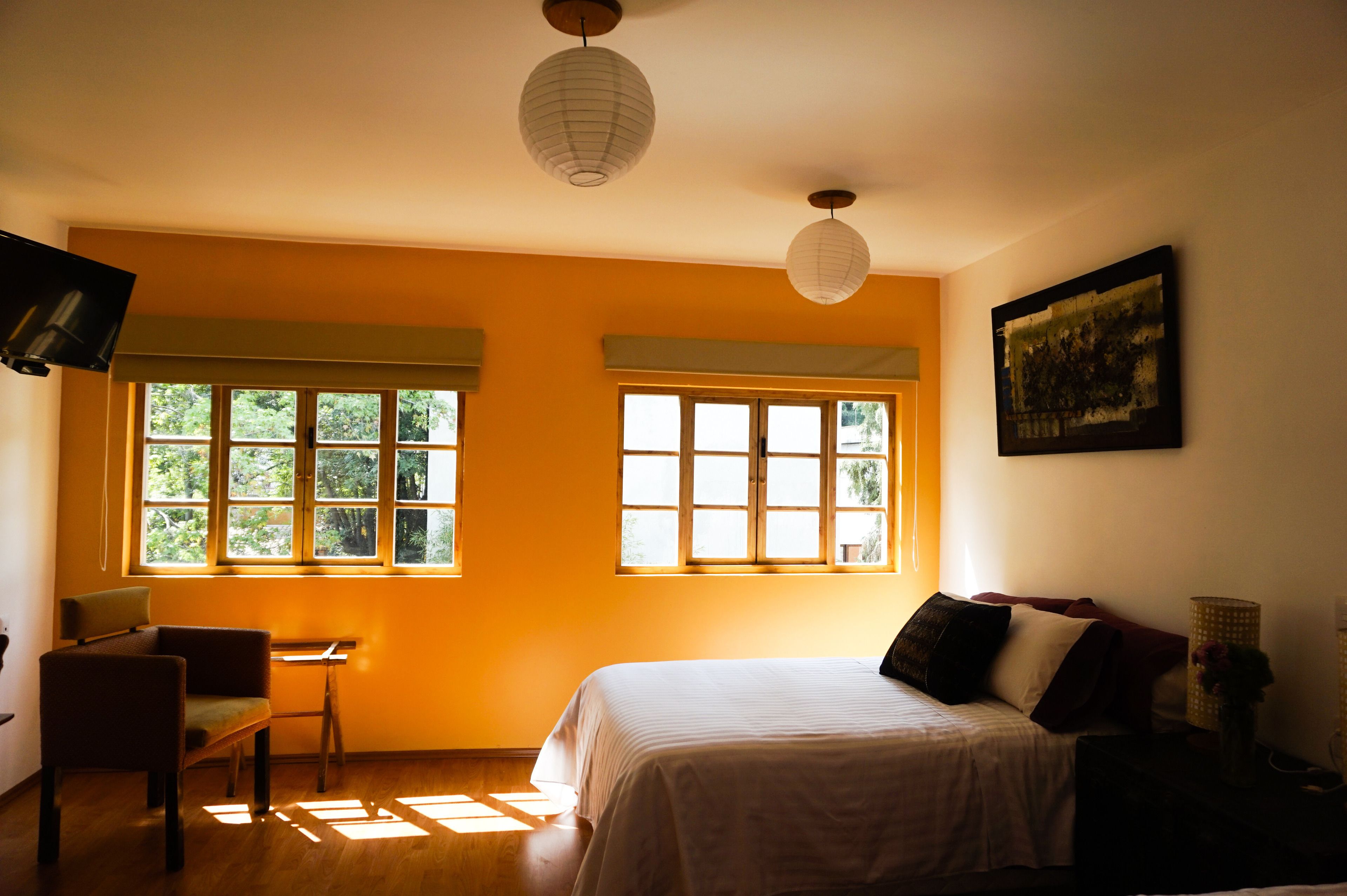 Ein Zimmer mit einem Bett, zwei Fenstern, einem Sessel, einem Tisch und einem Bild an der Wand.