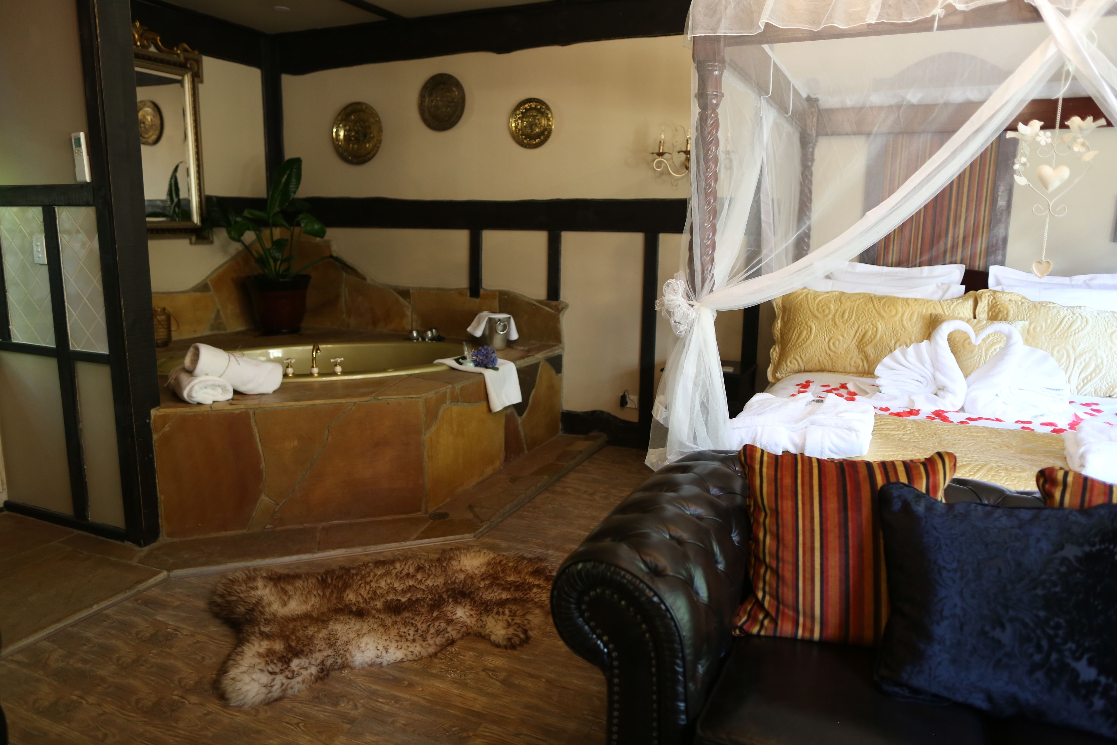 Una habitación con una bañera grande, una cama con ropa de cama blanca y dorada, un sofá de cuero y una alfombra de piel en el suelo.