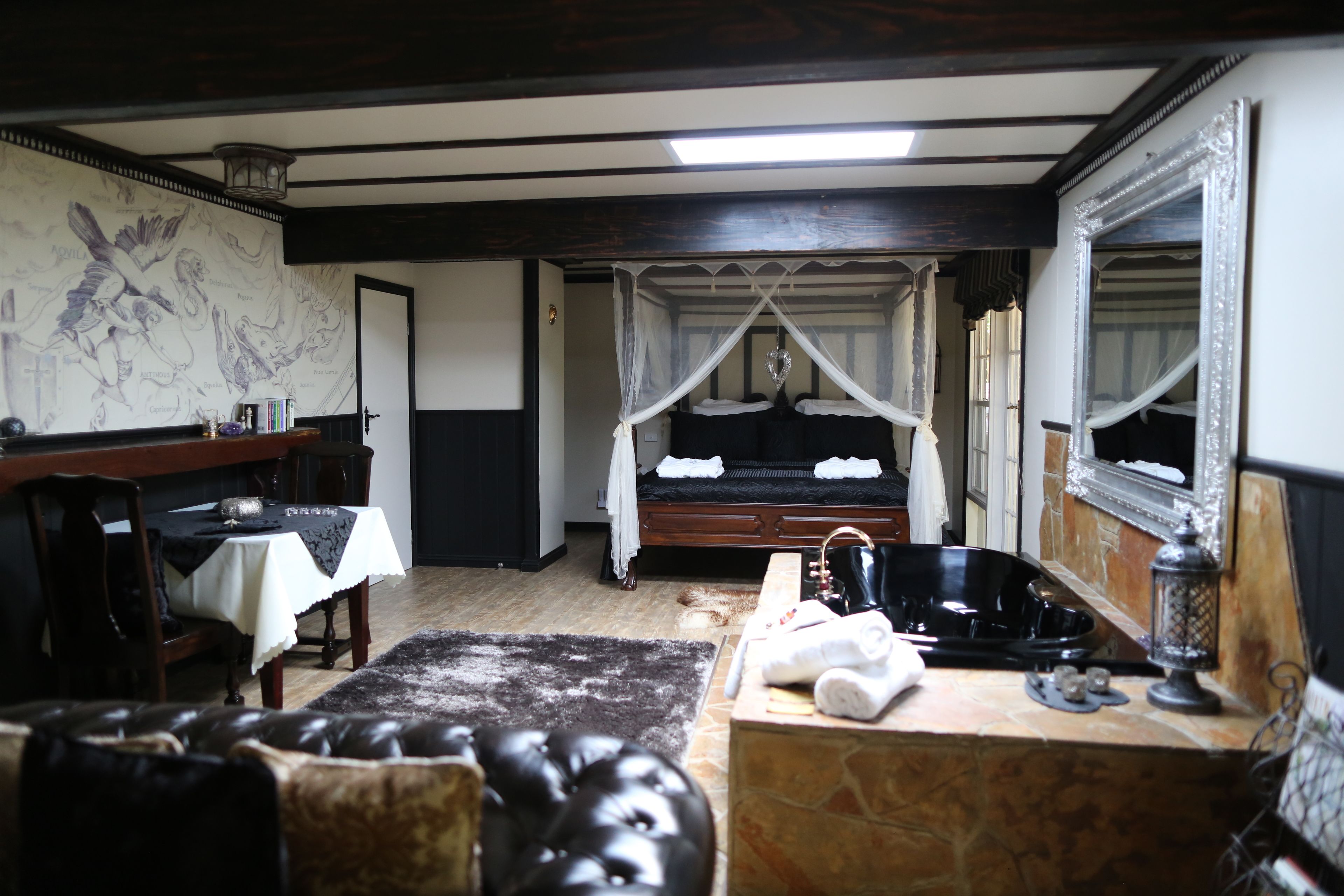 A bedroom with a canopy bed, a stone counter, a mirror, and a dining area with a table and chairs.