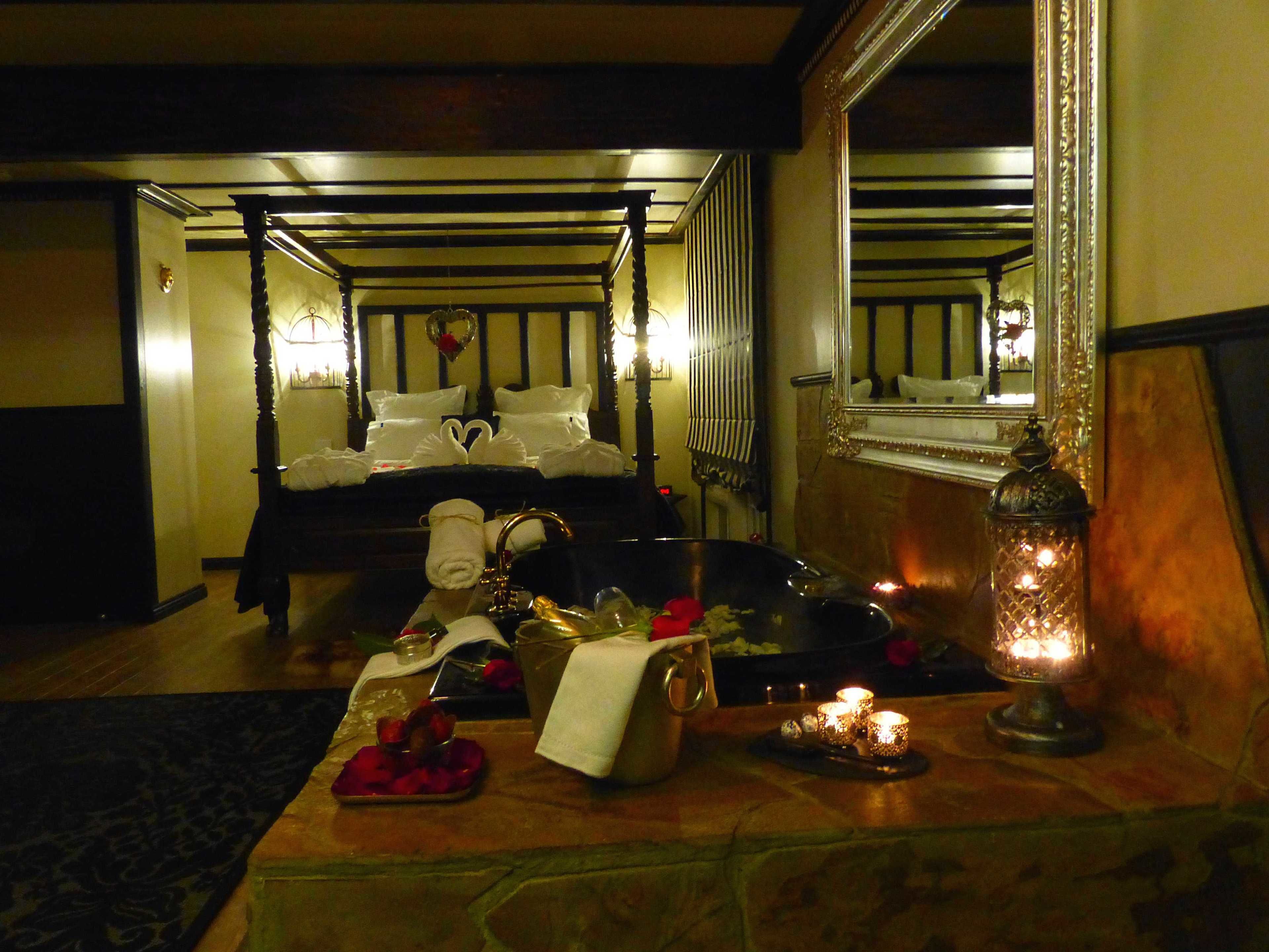 A dimly lit room with a bed, a large mirror, and a table with candles and a tray of fruit.