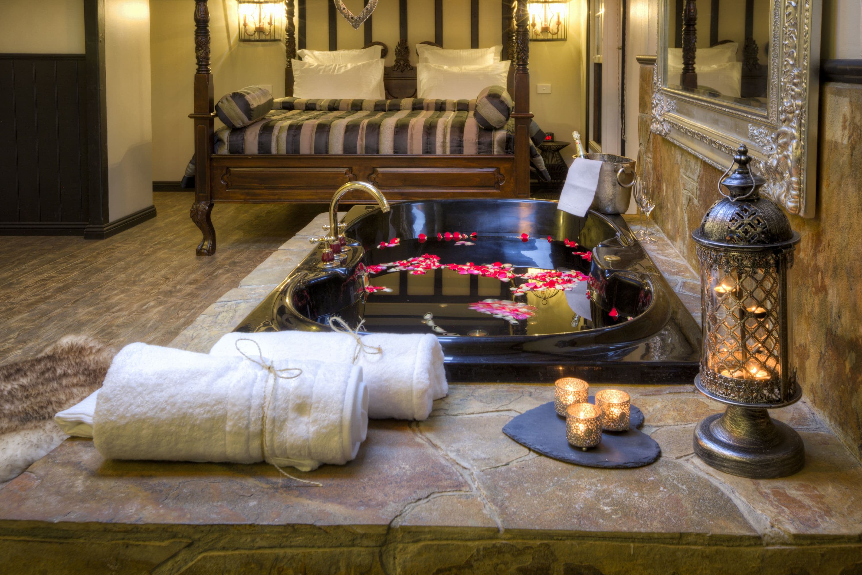 A bathroom with a stone sink, a bathtub with rose petals, a bench, and a mirror.