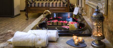 A bathroom with a stone sink, a bathtub with rose petals, a bench, and a mirror.