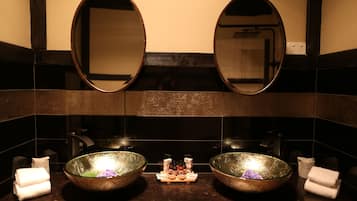 A bathroom with two large oval mirrors, a central sink with a decorative bowl, and towels on the counter.