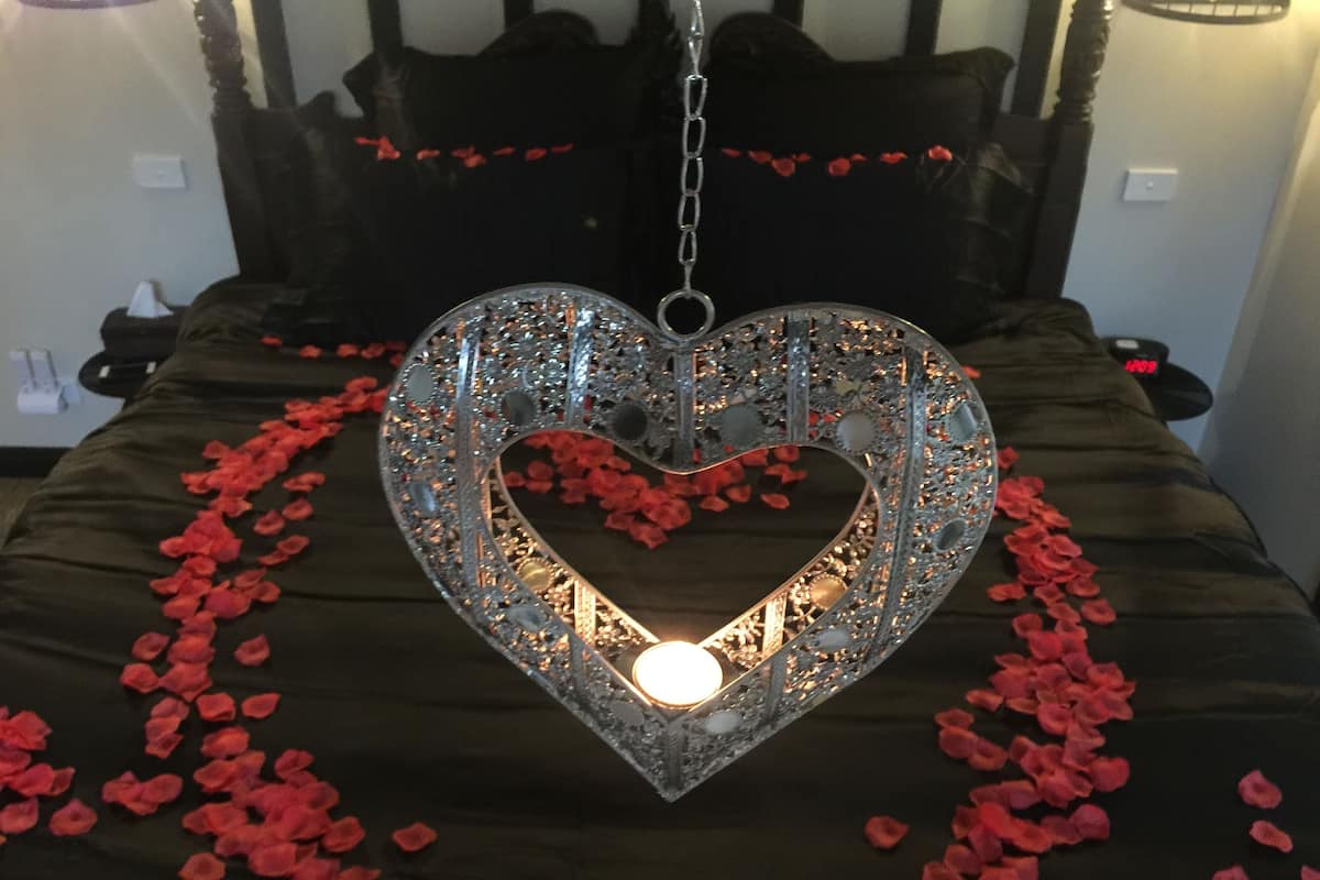 A bed with a heart-shaped light fixture in the center, surrounded by rose petals.